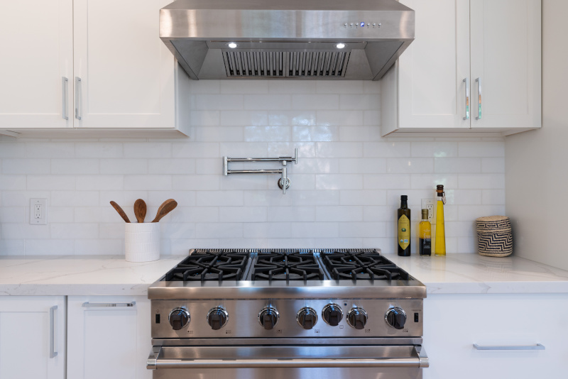 a gas stove with a range hood fan in a kitchen with white cabinets. Son-Rise Plumbing can help Calgarians upgrade to a gas stove from an electric stove.